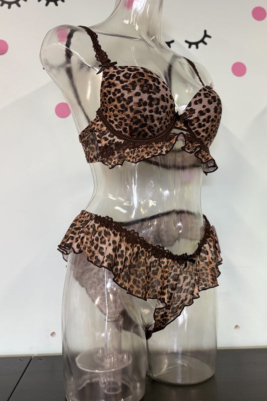 A two-piece leopard print lingerie set displayed on a clear mannequin torso. The set features a ruffled underwire bra and matching ruffled high-waisted briefs in a brown, beige, and black leopard pattern with dark brown trim.