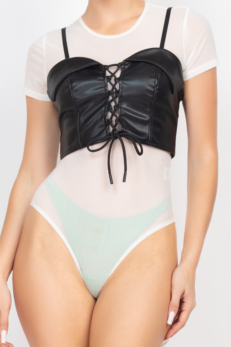 Person wearing a black lace-up bodysuit over a white top on a light gray background