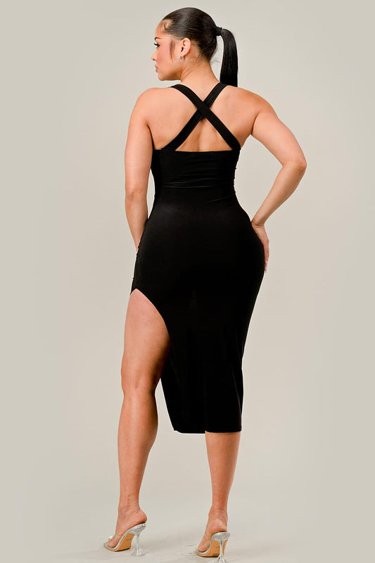 Woman wearing a black dress with criss-cross straps and a slit on a plain background