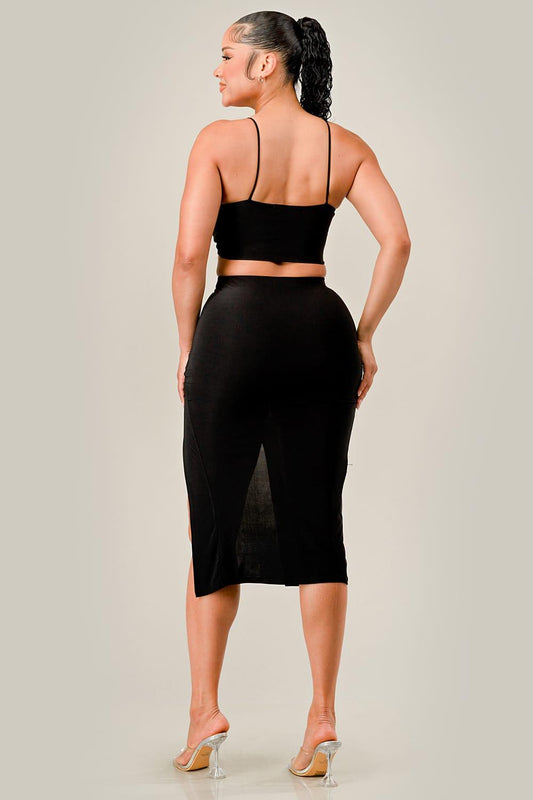 Woman wearing a black open-back top and skirt set on a plain background