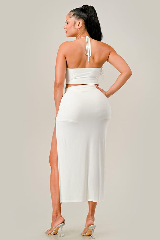 Woman wearing an off white outfit with a high slit on a plain background