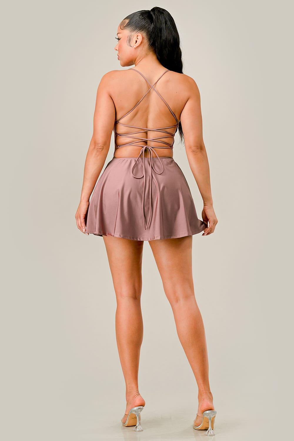Woman wearing a rose gold dress with thin straps and open back on a plain background