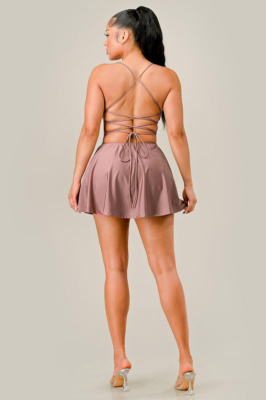 Woman wearing a rose gold dress with thin straps and open back on a plain background