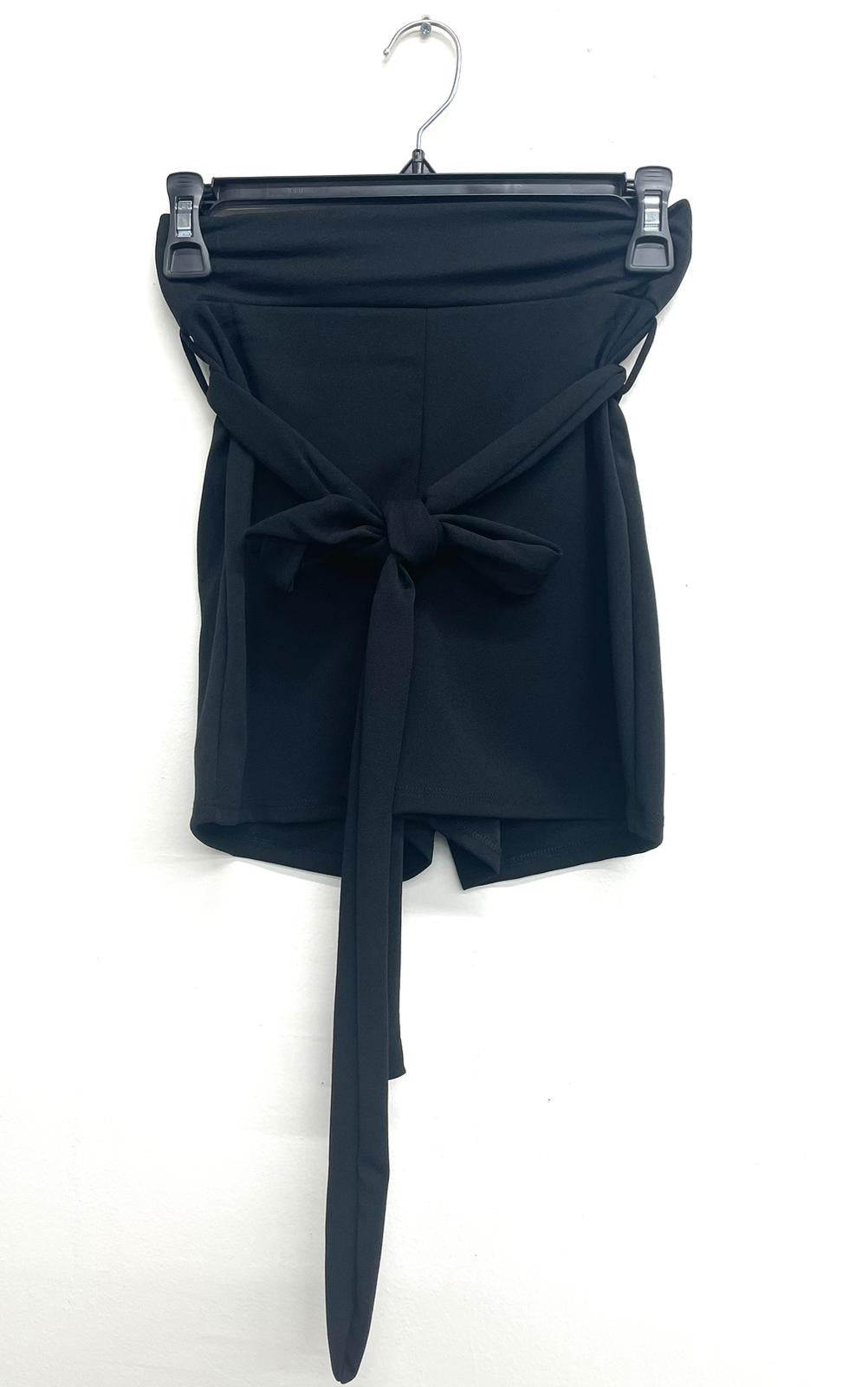 Black shorts with a wide belt on a hanger against a white background