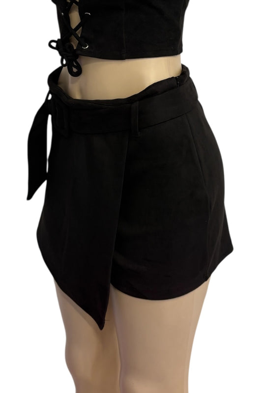 Black wrap-style shorts with a tie belt and asymmetrical hem, shown on a mannequin torso against a plain white background.