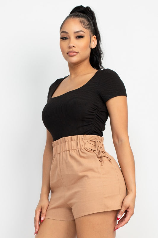 Woman wearing a black top and tan shorts on a white background