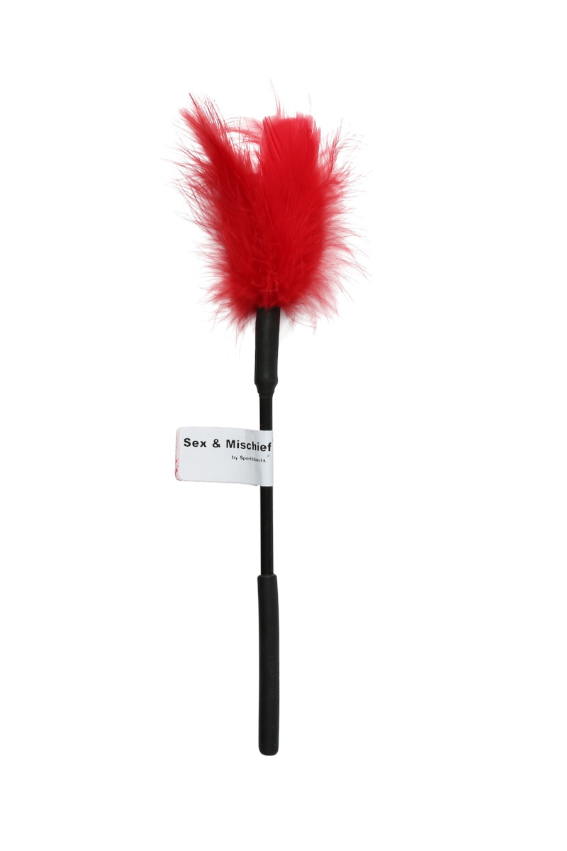 A red feather duster with a black handle and a white paper tag that reads 'Sex & Mischief' on a plain white background.