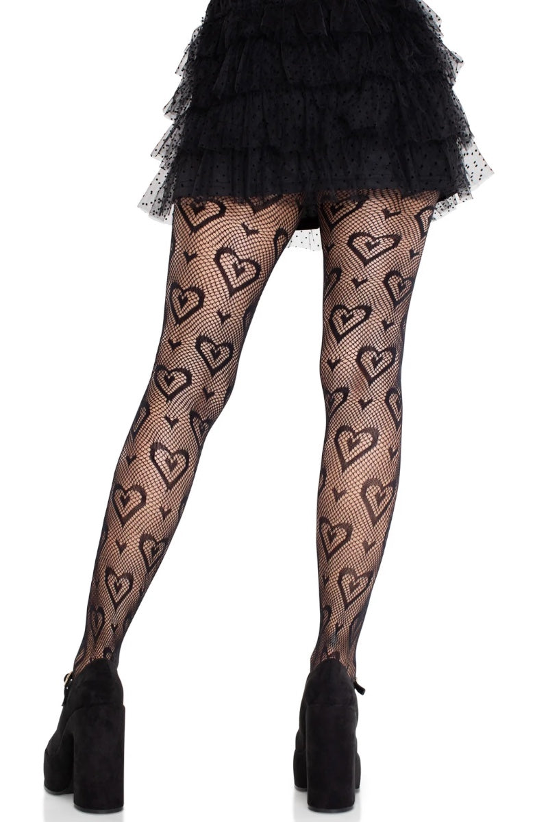 Black heart-patterned fishnet tights worn by a model, paired with a black ruffled skirt and black platform boots, shown from the waist down on a white background.