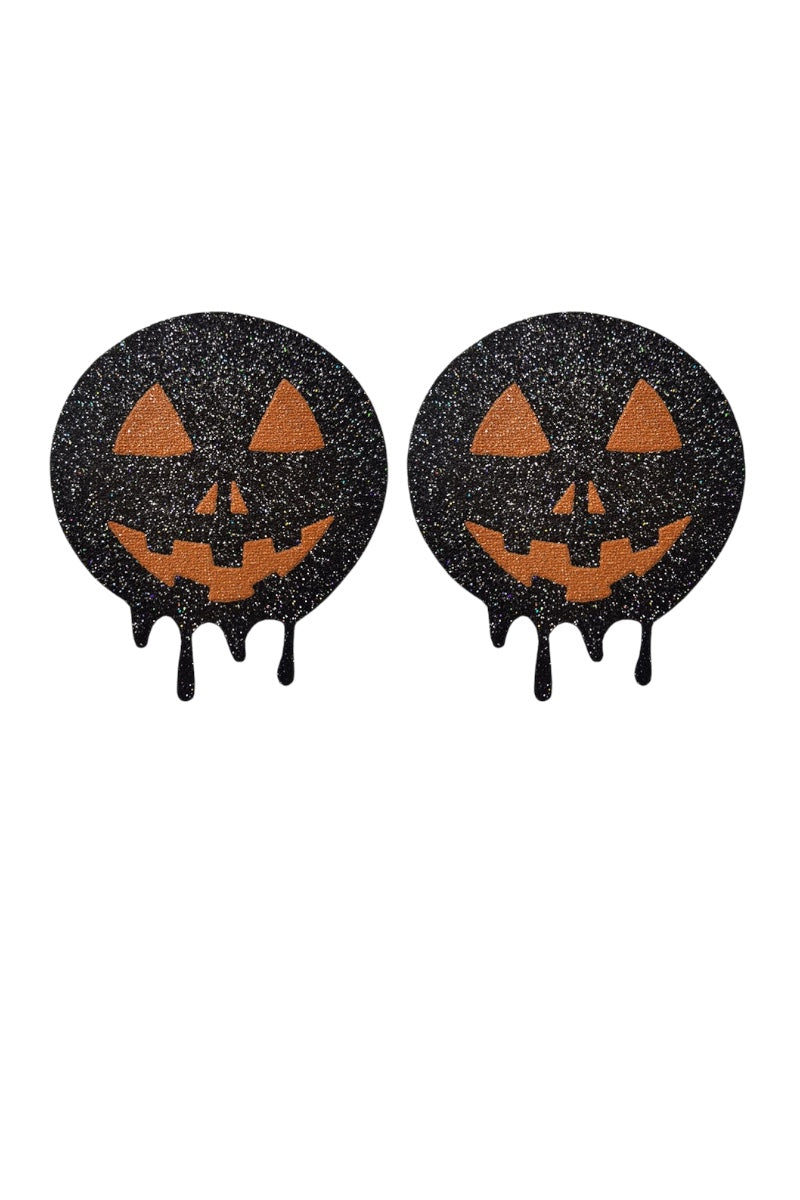 Two black glittery Halloween pasties with jack-o'-lantern faces on a white background.
