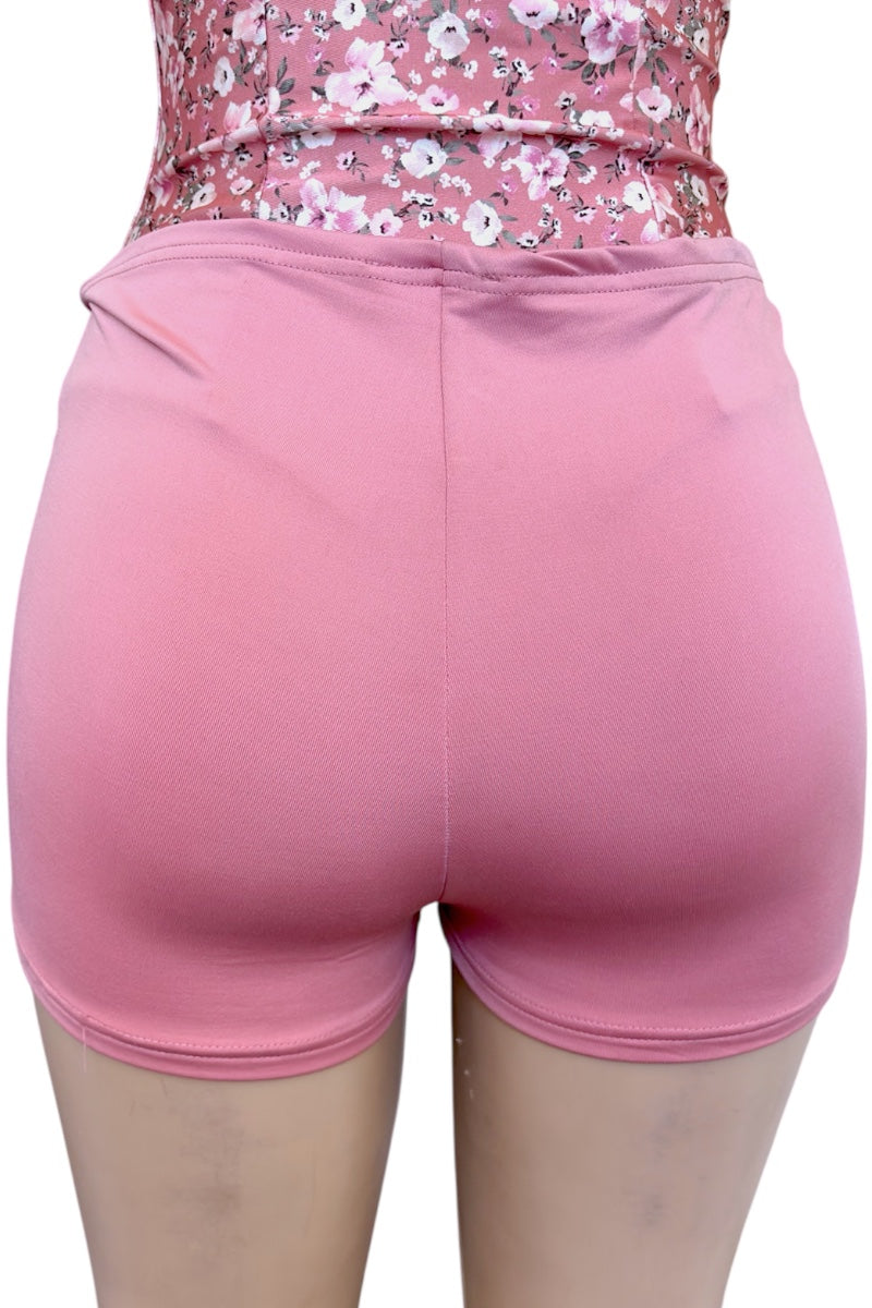 Pink shorts worn over a floral top on a white background