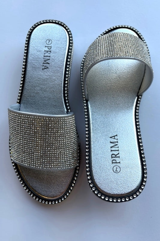 Silver embellished sandals with 'Prima' branding on a light blue background