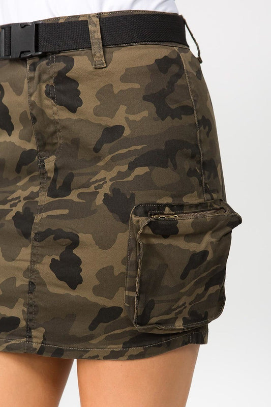 Close-up of a camouflage cargo mini skirt with a black belt and side cargo pocket, worn by a model.