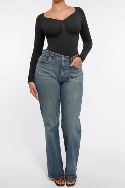Person wearing a black long-sleeve top and blue jeans on a white background