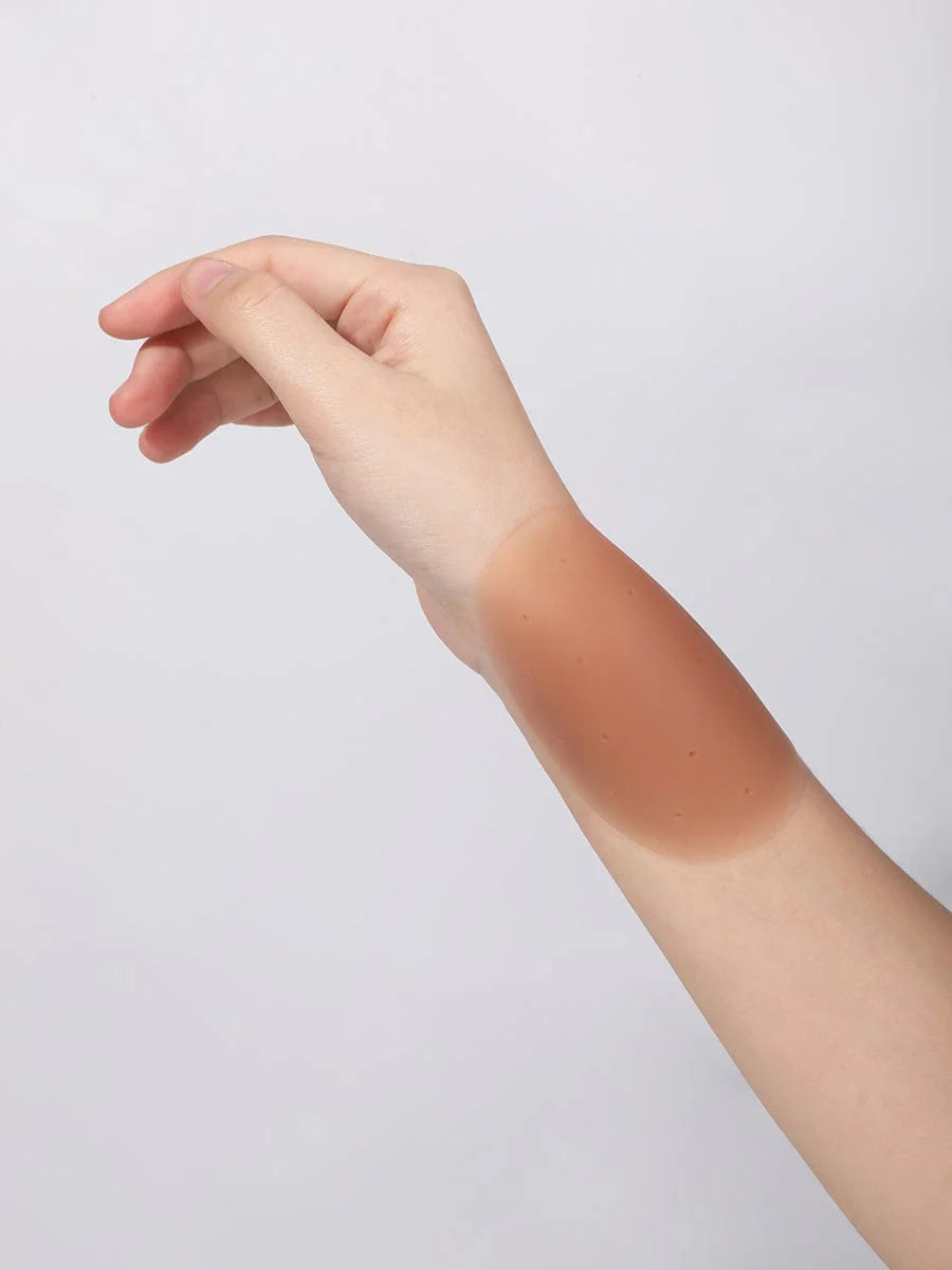 Hand and arm with a tan nipple cover on a light gray background