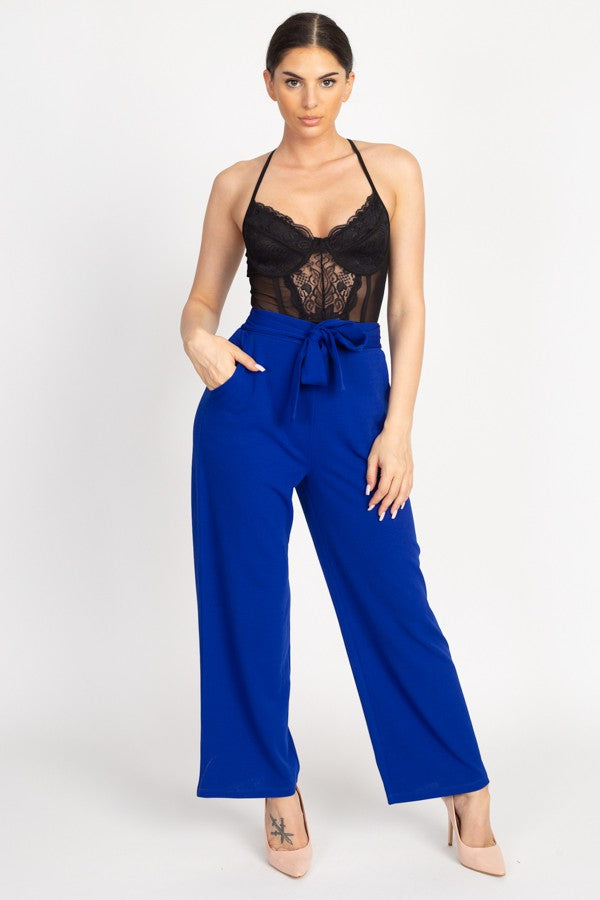 Woman wearing a black lace top and blue high-waisted pants on a white background
