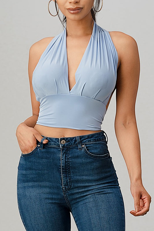 Woman wearing a serenity blue halter top and blue jeans against a gray background