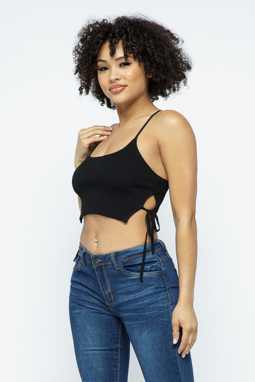 Woman wearing a black crop top with cut-out design and blue jeans on a white background