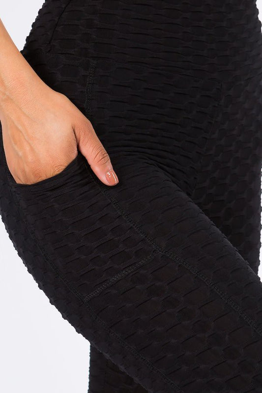 Close-up of textured black leggings with a hand in the pocket on a white background