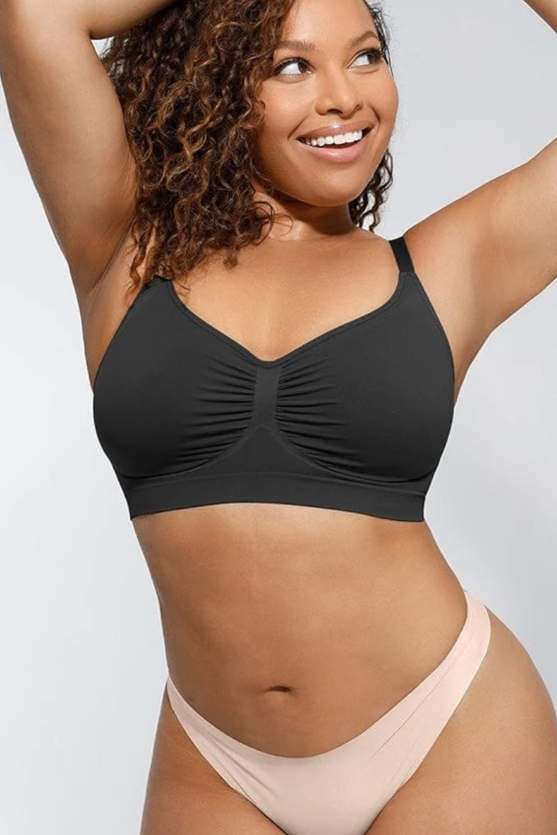 Woman wearing a black bralette and beige bottoms against a light gray background
