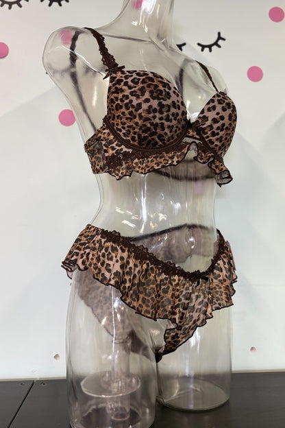 A two-piece leopard print lingerie set displayed on a clear mannequin torso. The set features a ruffled underwire bra and matching ruffled high-waisted briefs in a brown, beige, and black leopard pattern with dark brown trim.