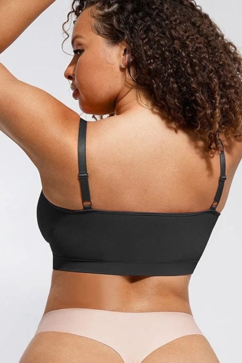 Woman wearing a black bralette and beige underwear on a plain background