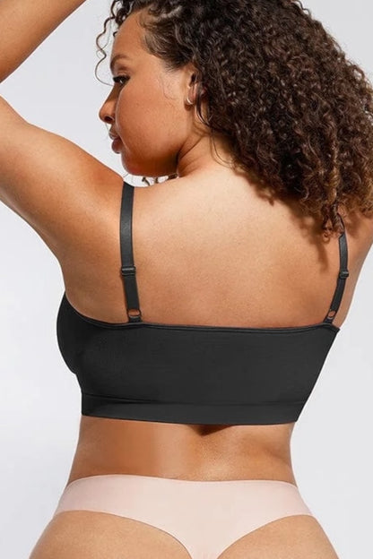 Woman wearing a black bralette and beige underwear on a plain background