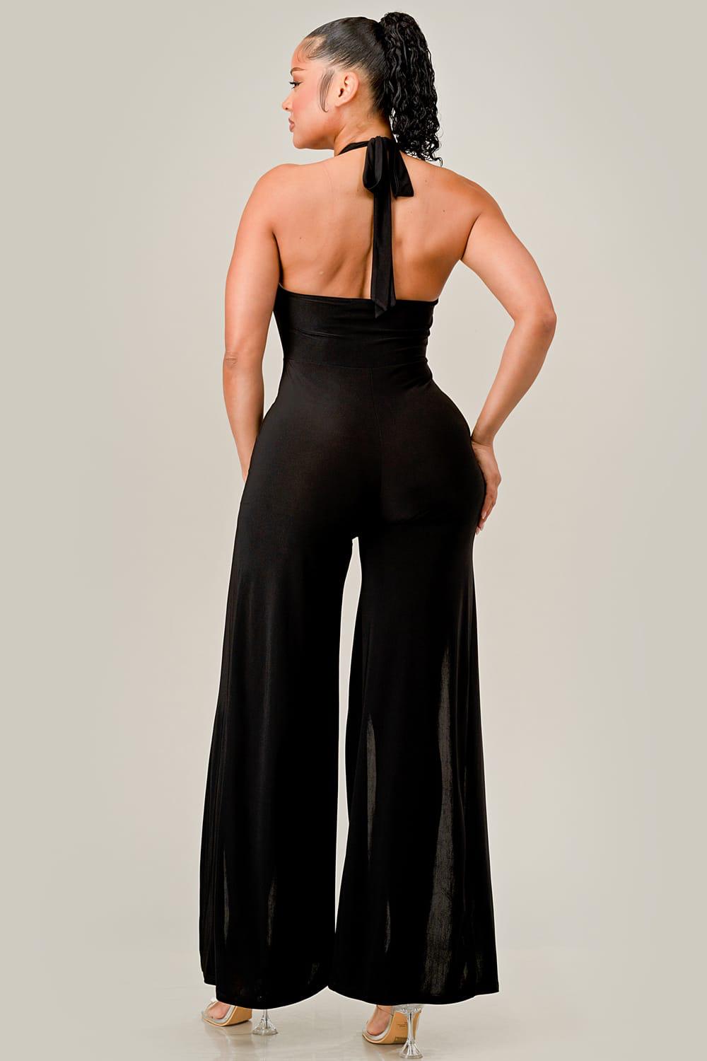 Woman wearing a black jumpsuit with a halter neck design on a plain background