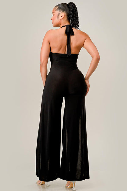 Woman wearing a black jumpsuit with a halter neck design on a plain background