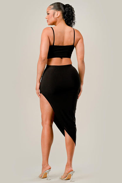 Woman wearing a black outfit with a slit skirt on a plain background