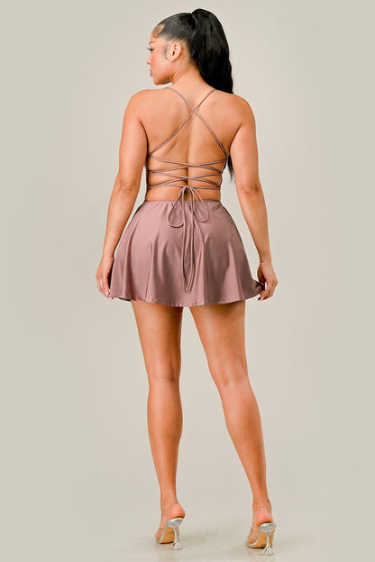 Woman wearing a rose gold dress with thin straps and open back on a plain background