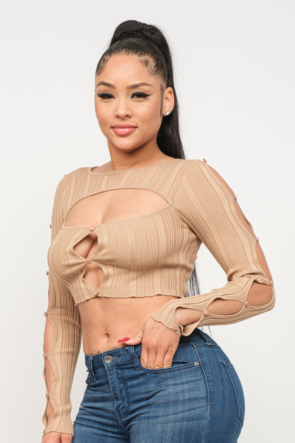 Woman wearing a long sleeve milk coffee color crop top with cut-out design and blue jeans on a white background