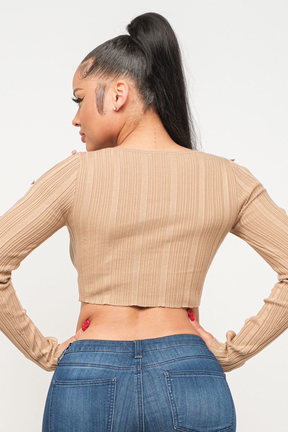 Woman wearing a long sleeve milk coffee color crop top and blue jeans on a white background