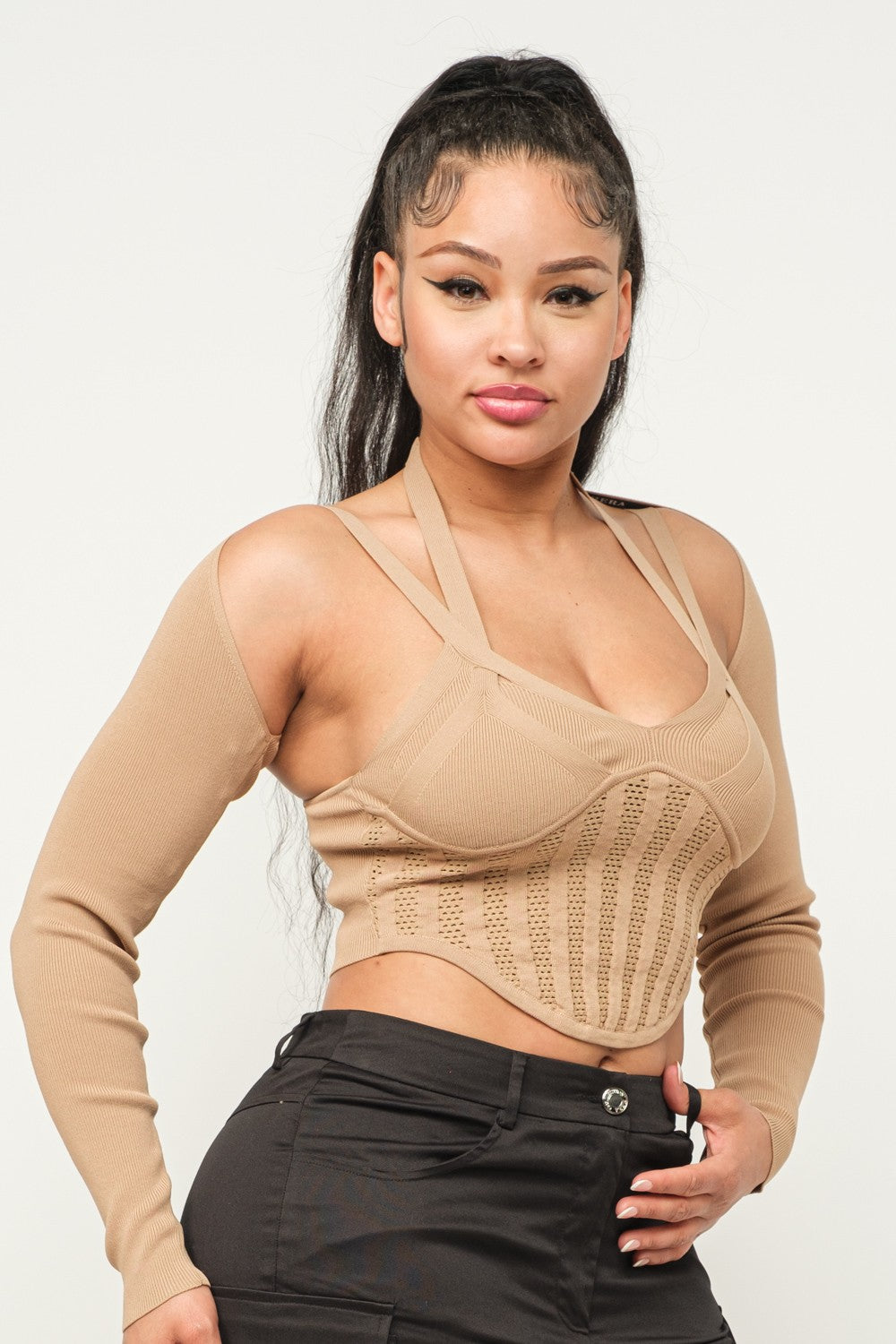 Woman wearing a long sleeve milk coffee color crop top with cut-out design and black pants on a white background