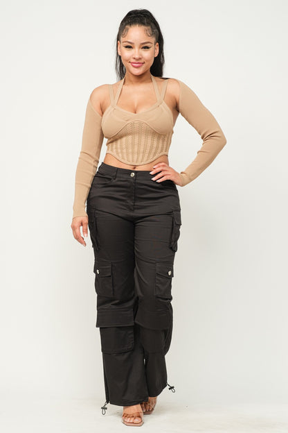 Woman wearing a long sleeve milk coffee color crop top with cut-out design and black pants on a white background