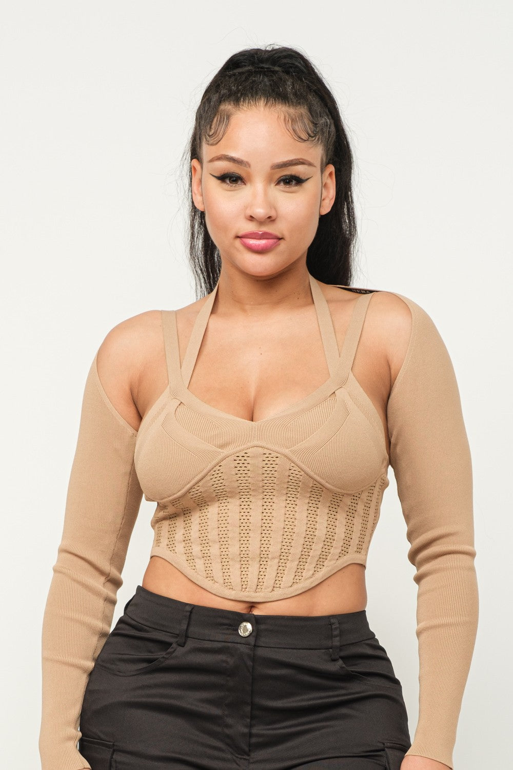 Woman wearing a long sleeve milk coffee color crop top with cut-out design and black pants on a white background
