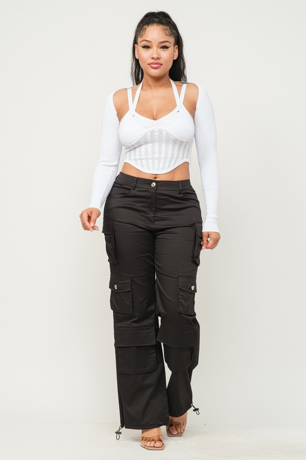Woman wearing a long sleeve white crop top with cut-out design and black pants on a white background