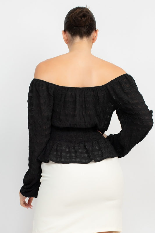 Black off-shoulder top worn by a person on a white background
