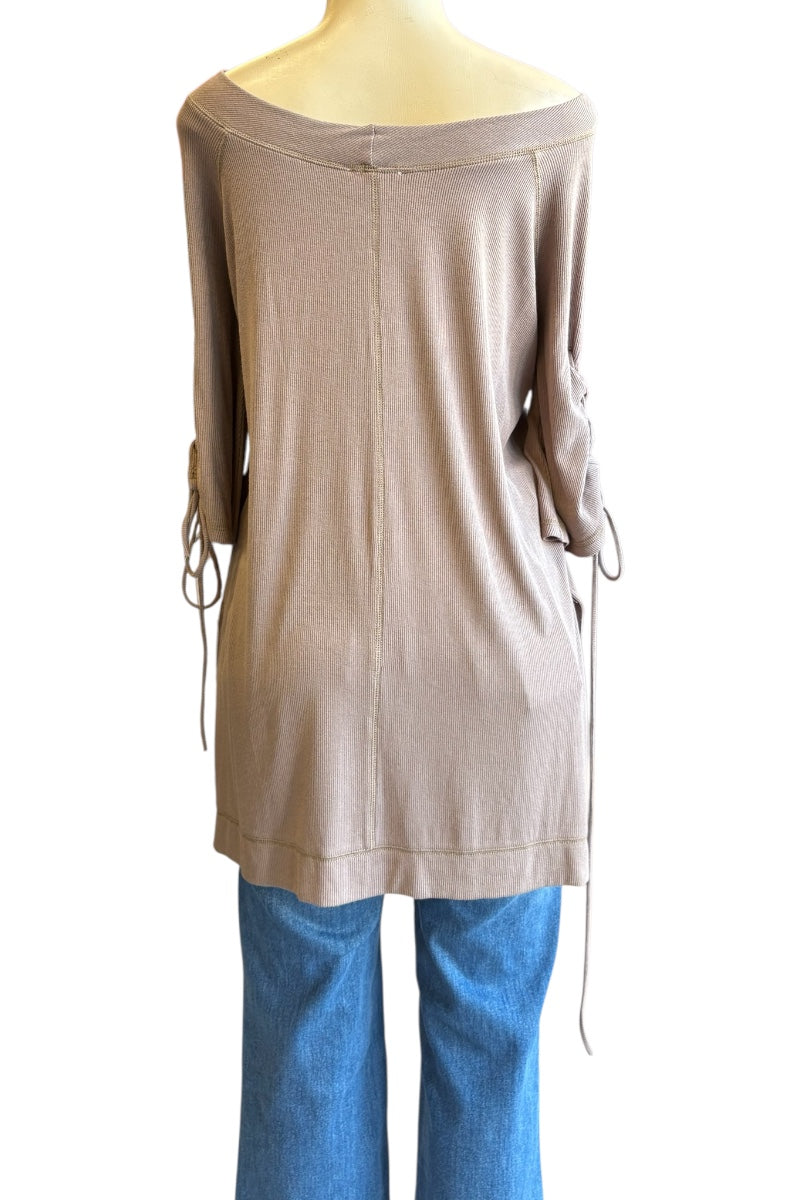 A taupe off-the-shoulder long-sleeve knit top with side tie details, displayed on a mannequin with blue jeans against a white background.
