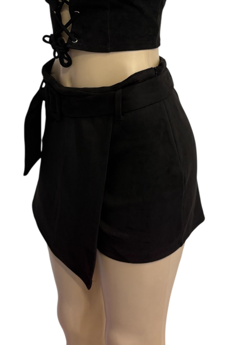 Black wrap-style shorts with a tie belt and asymmetrical hem, shown on a mannequin torso against a plain white background.