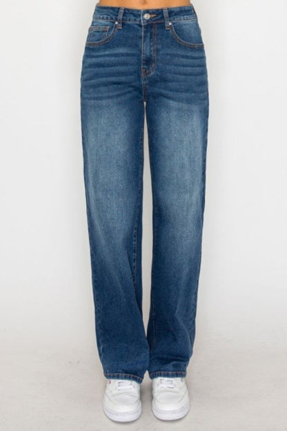 A person wearing high-waisted, wide-leg blue denim jeans with white sneakers, shown from the waist down against a plain light gray studio background.