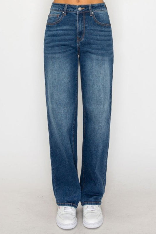A person wearing high-waisted, wide-leg blue denim jeans with white sneakers, shown from the waist down against a plain light gray studio background.