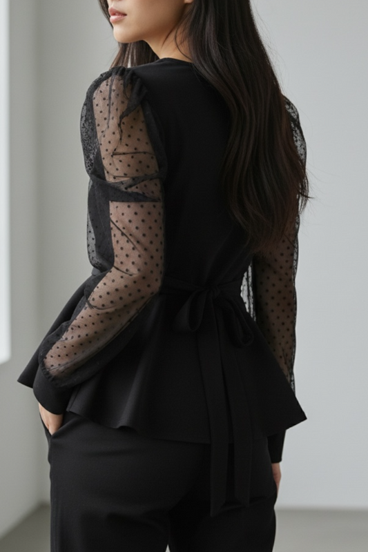 Person wearing a black outfit with sheer sleeves against a plain background