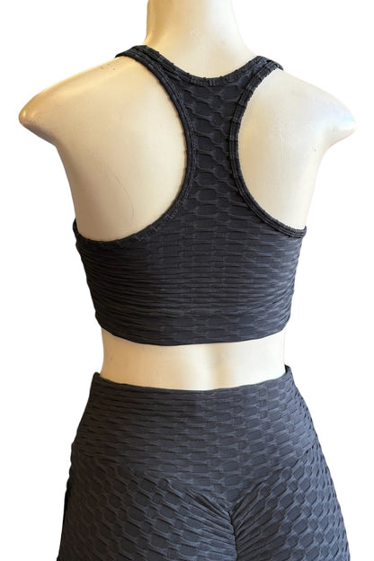 Black textured sports bra and matching high-waisted leggings set displayed on a mannequin from the back, showing a honeycomb-like pattern and racerback design.