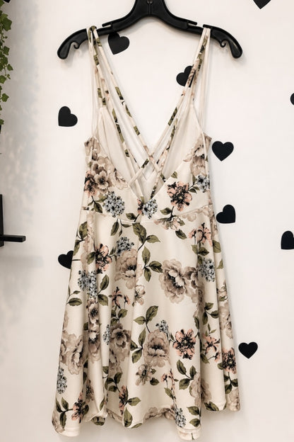 A sleeveless cream-colored slip dress with a floral print, hanging on a black hanger against a white wall decorated with black heart stickers.