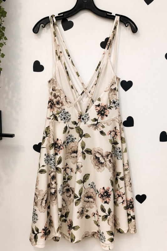 A sleeveless cream-colored slip dress with a floral print, hanging on a black hanger against a white wall decorated with black heart stickers.