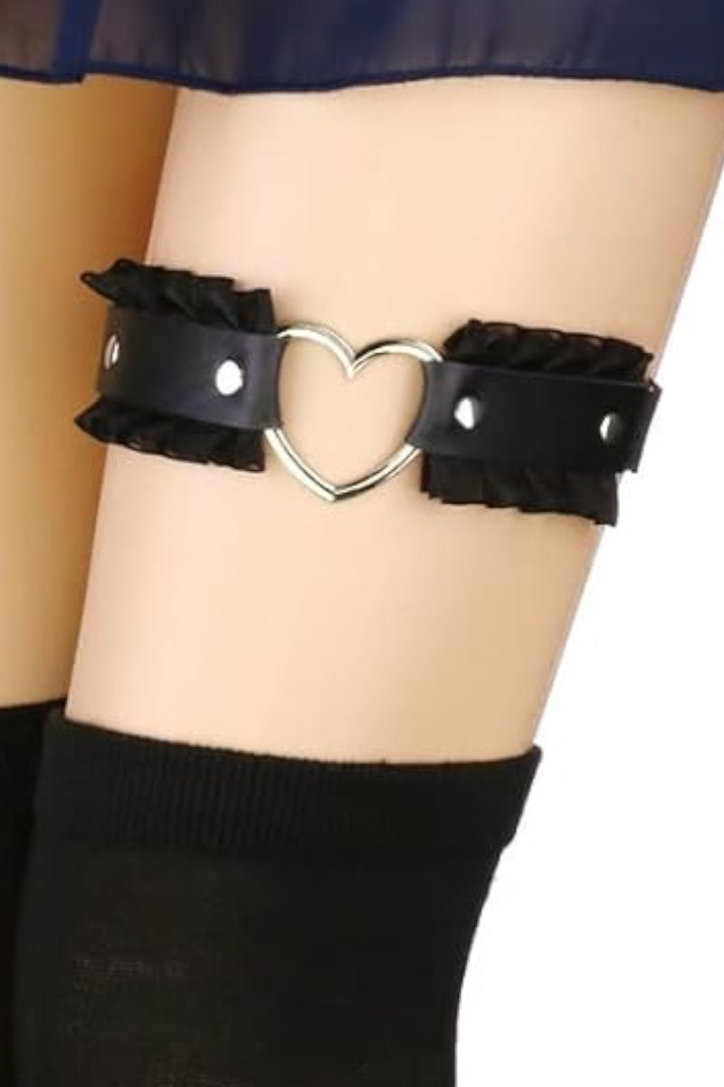 A black faux-leather thigh strap with ruffled edges and a central silver heart-shaped metal clasp, shown worn on a person's leg with black socks visible below.