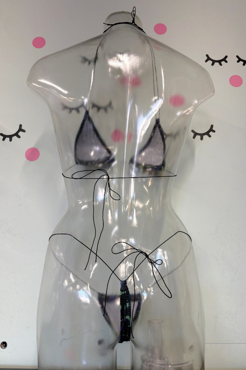 A transparent mannequin torso wearing a sheer black string bikini with sheer cups, photographed against a white wall with pink polka dots and eyelash decals.