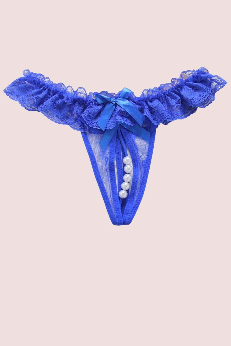 Blue lace thong with a ruffled waistband, sheer mesh front, a blue satin bow, and a vertical row of white faux pearls down the center, shown on a solid pale pink background.