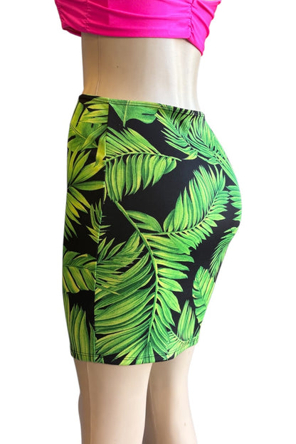 A mannequin torso wearing a fitted mini skirt with a bold green tropical leaf print on a black background, paired with a bright pink cropped top against a plain white studio background.
