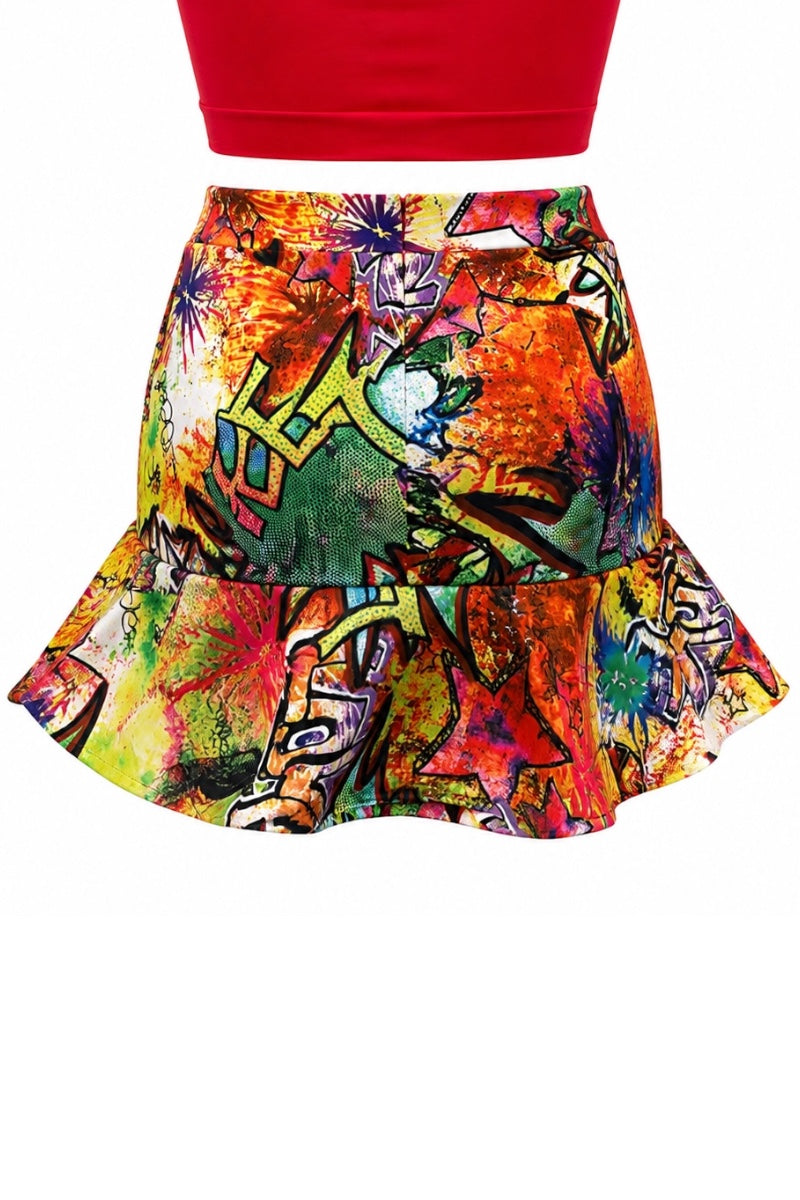 A colorful ruffled mini skirt with a vibrant graffiti and paint splatter print, shown on a model cropped at the waist wearing a red top.